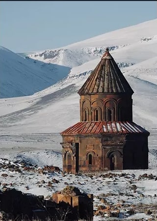 Karlı dağların önünde tek başına duran tarihi taş yapı